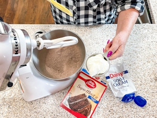 a person about to add sour cream into a mixer with boxed cake mix inside