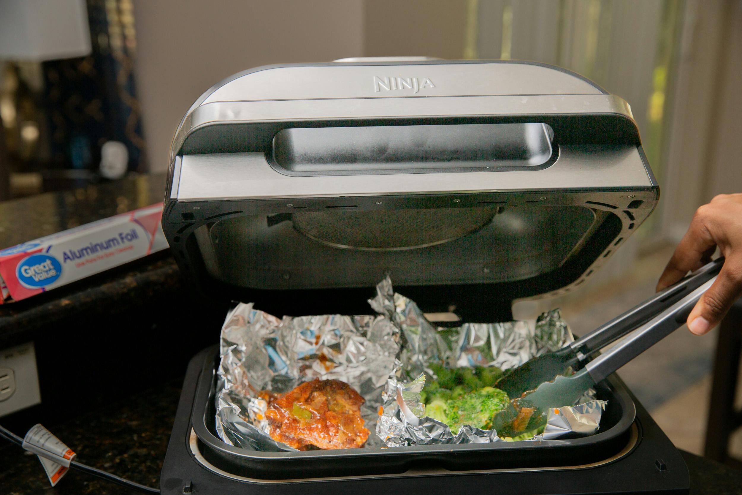 Airfryer with foil containing meat and broccolio
