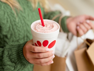 A person holding a Chick-fil-A peppermint milkshake and some bags