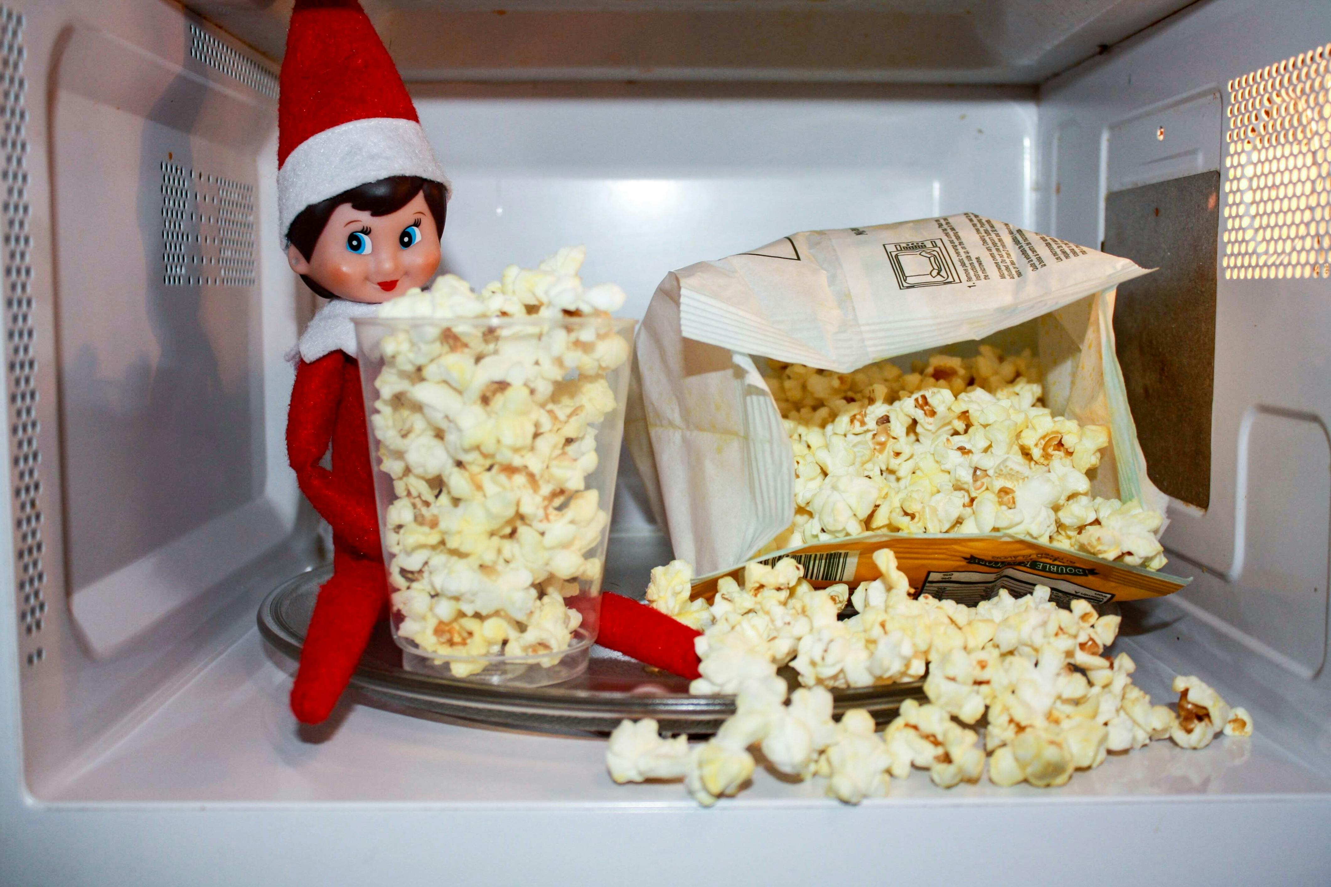 Elf on the shelf in a microwave with popcorn.