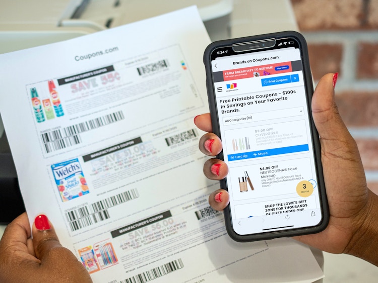 person holding phone with coupons.com brands and offers and printed coupons