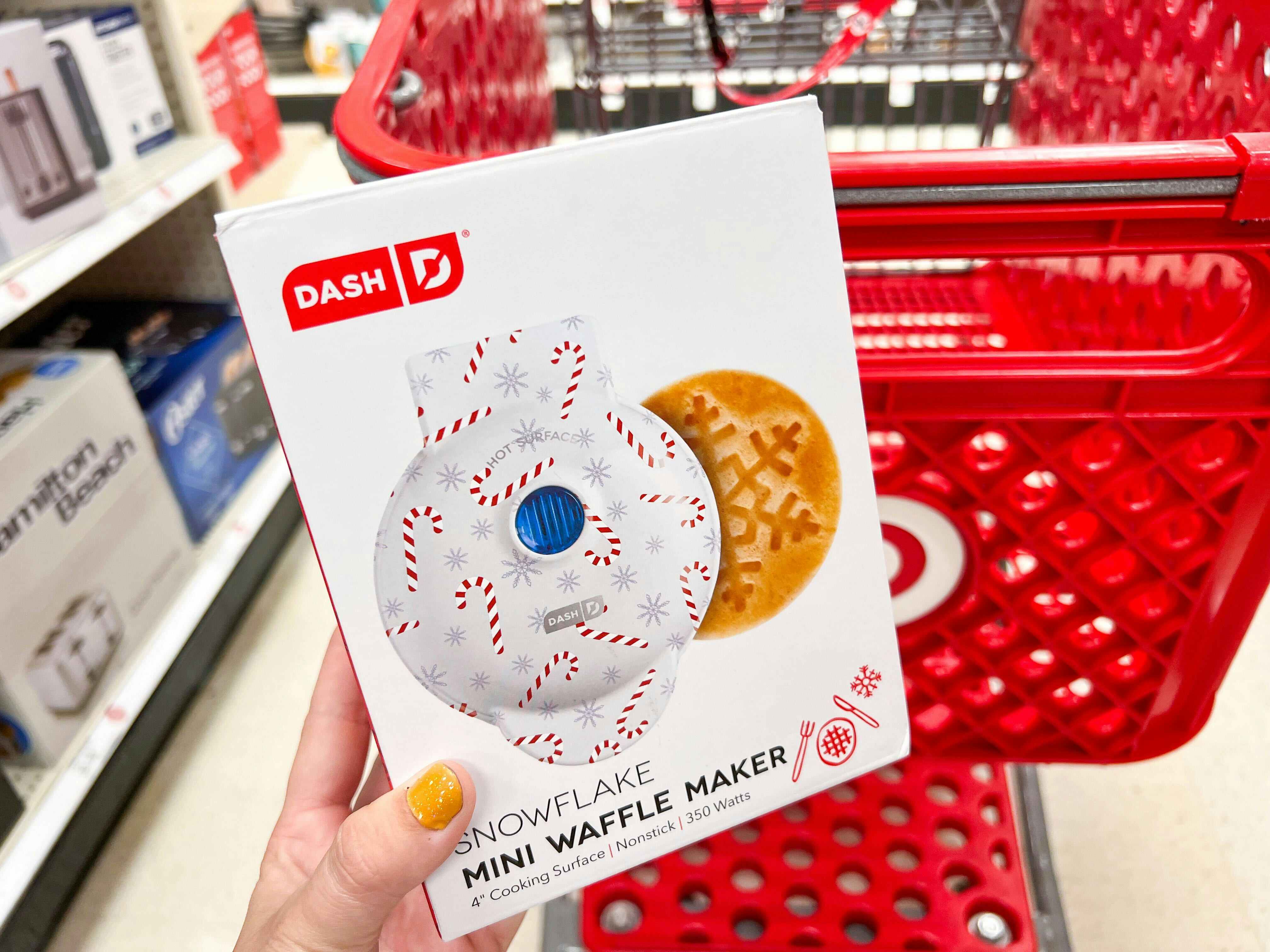 hand holding a dash snowflake mini waffle maker in front of a target cart