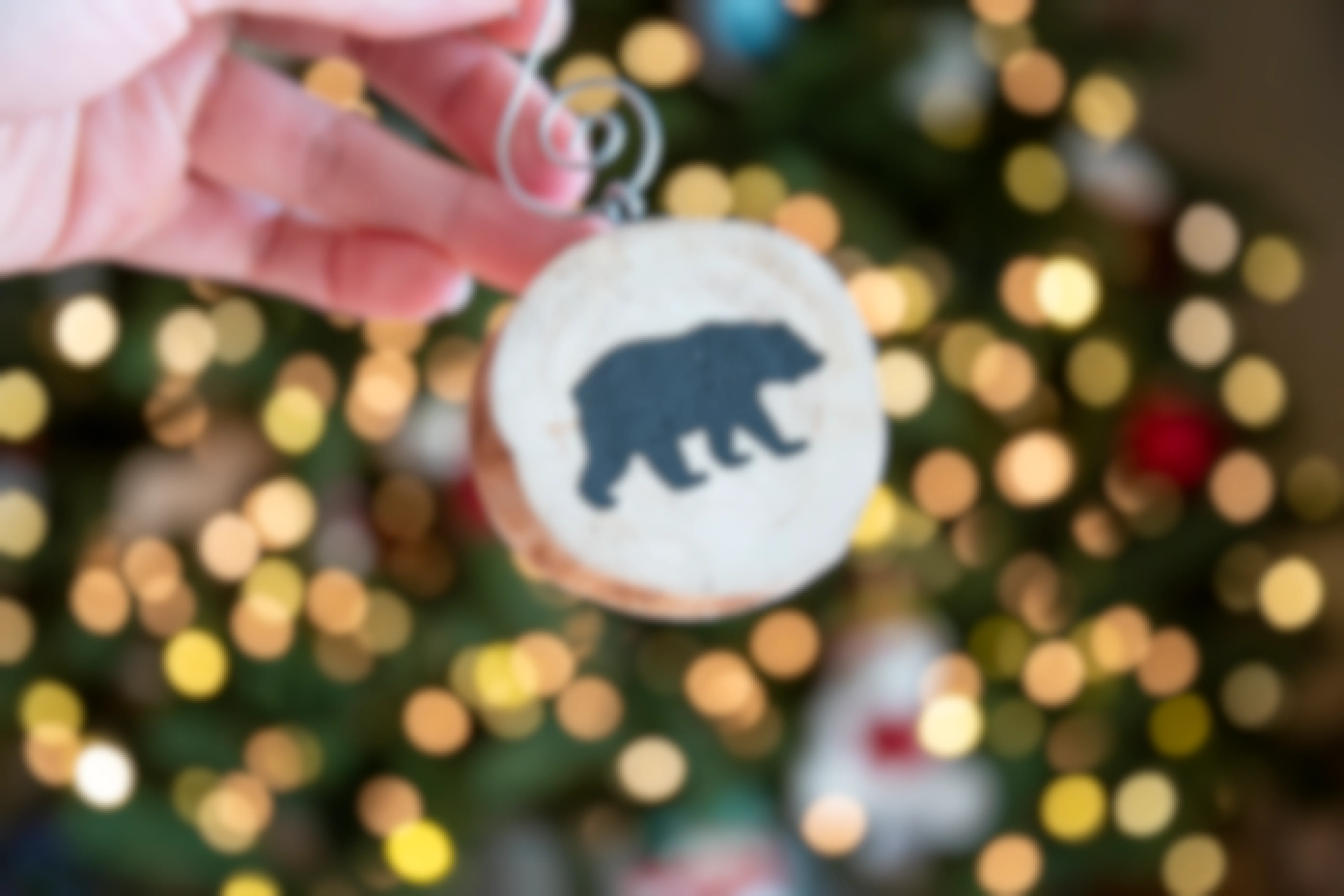 A person holding a wood slice ornament with a stencil of a black bear on the front of it.