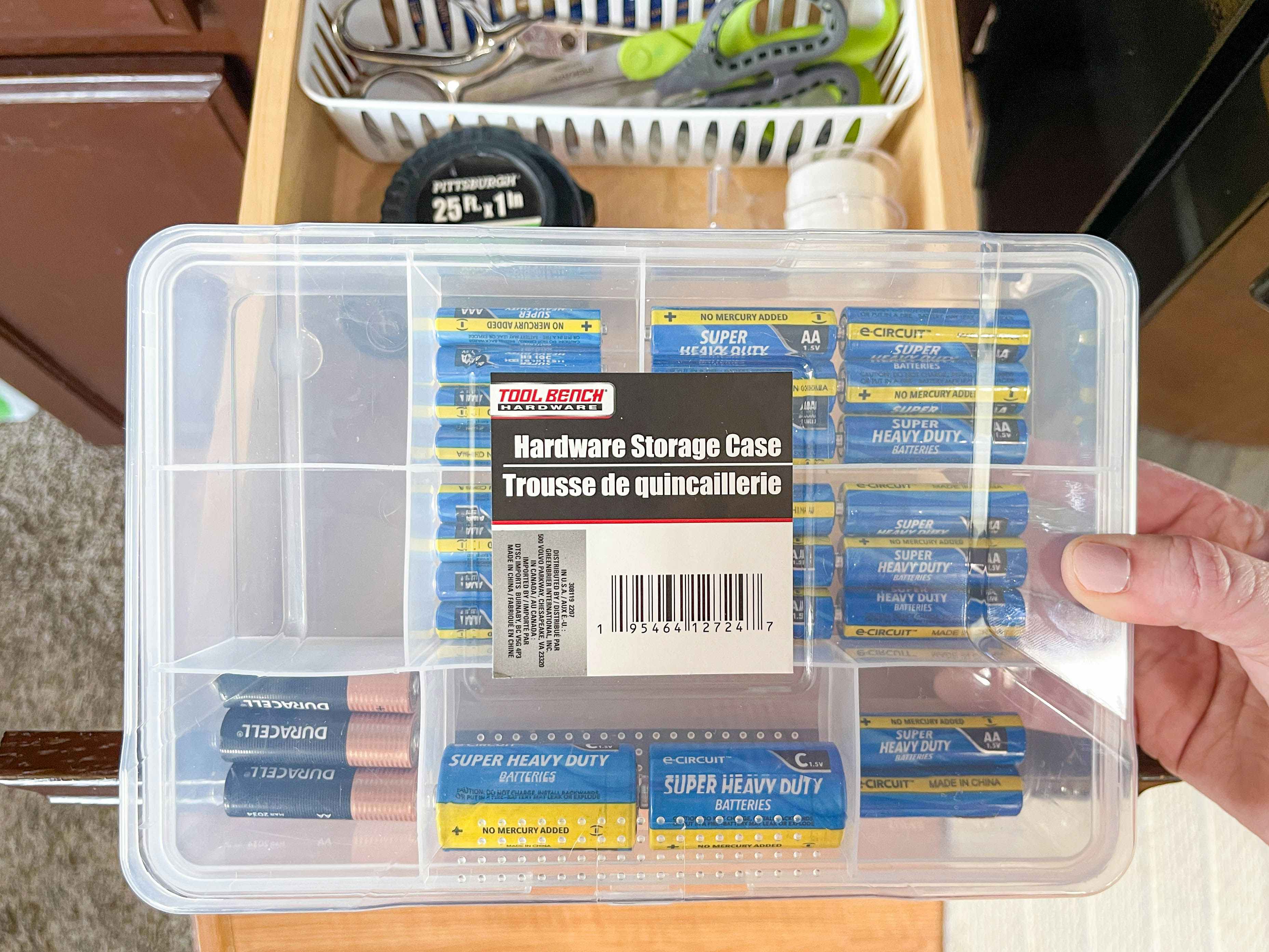 a person's hand holding a dollar tree hardware storage case with batteries inside 