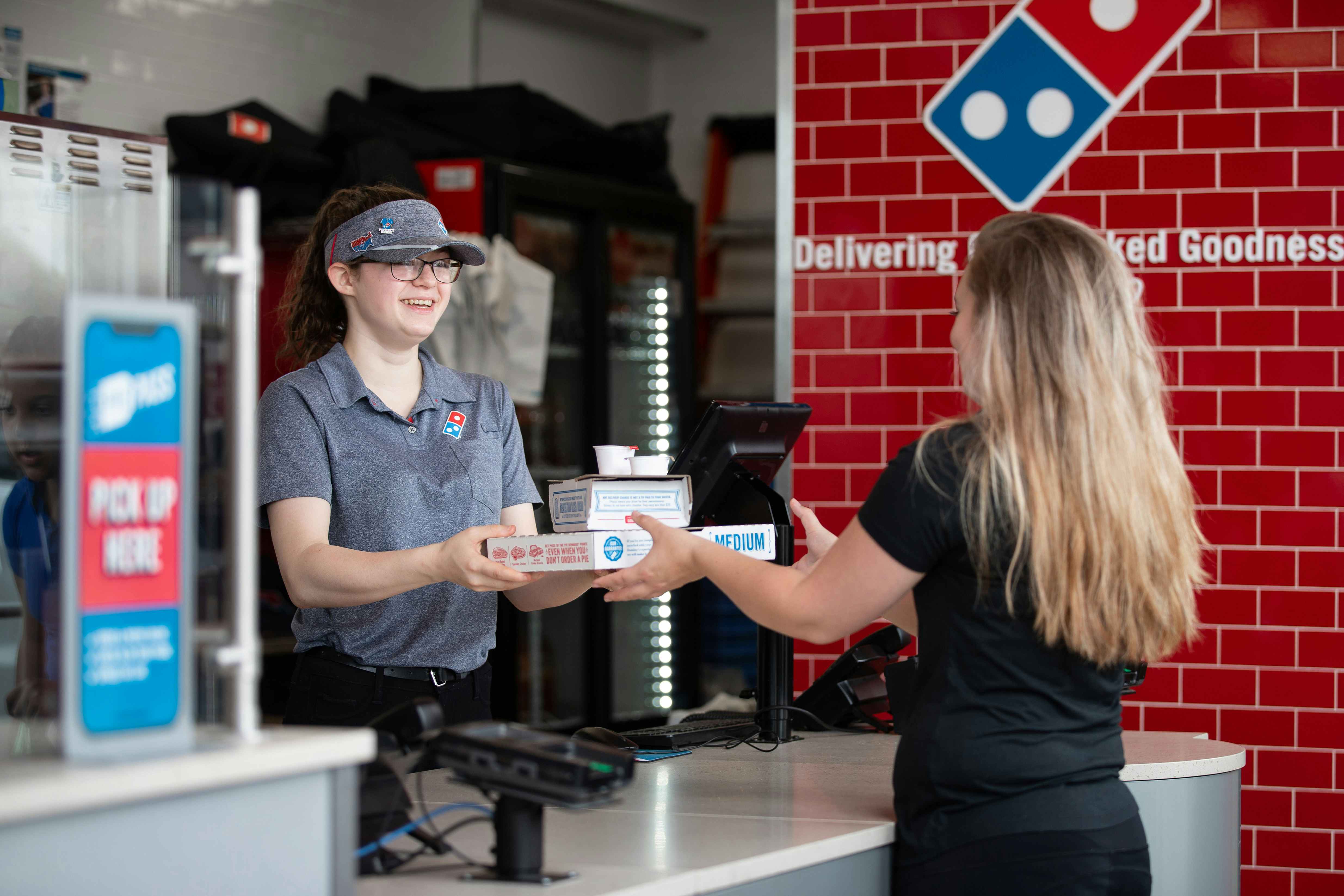 A customer receiving a pizza over the counter from a Domino's employee