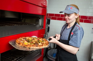 A Domino's employee taking a pizza out of the oven.