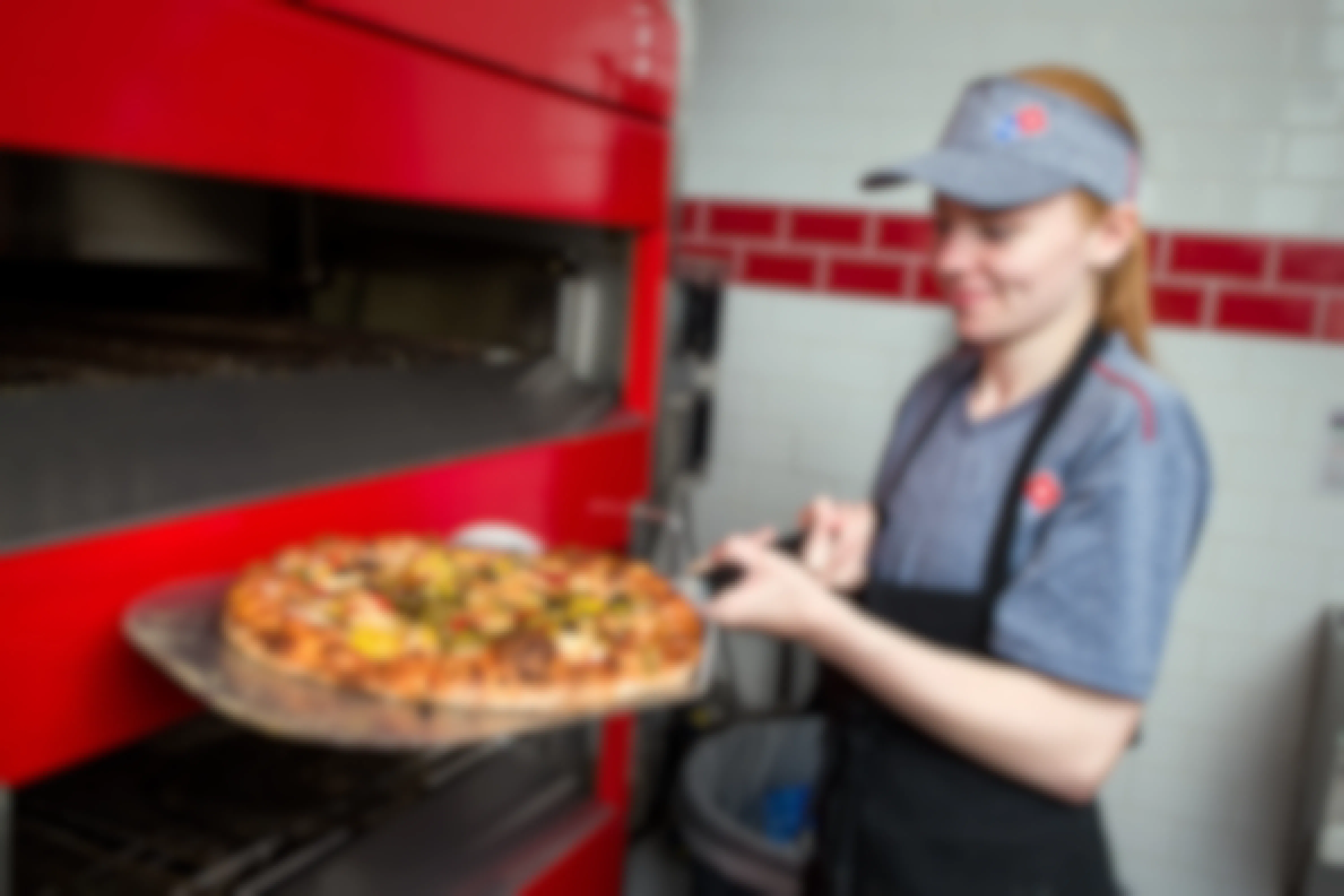A Domino's employee taking a pizza out of the oven.