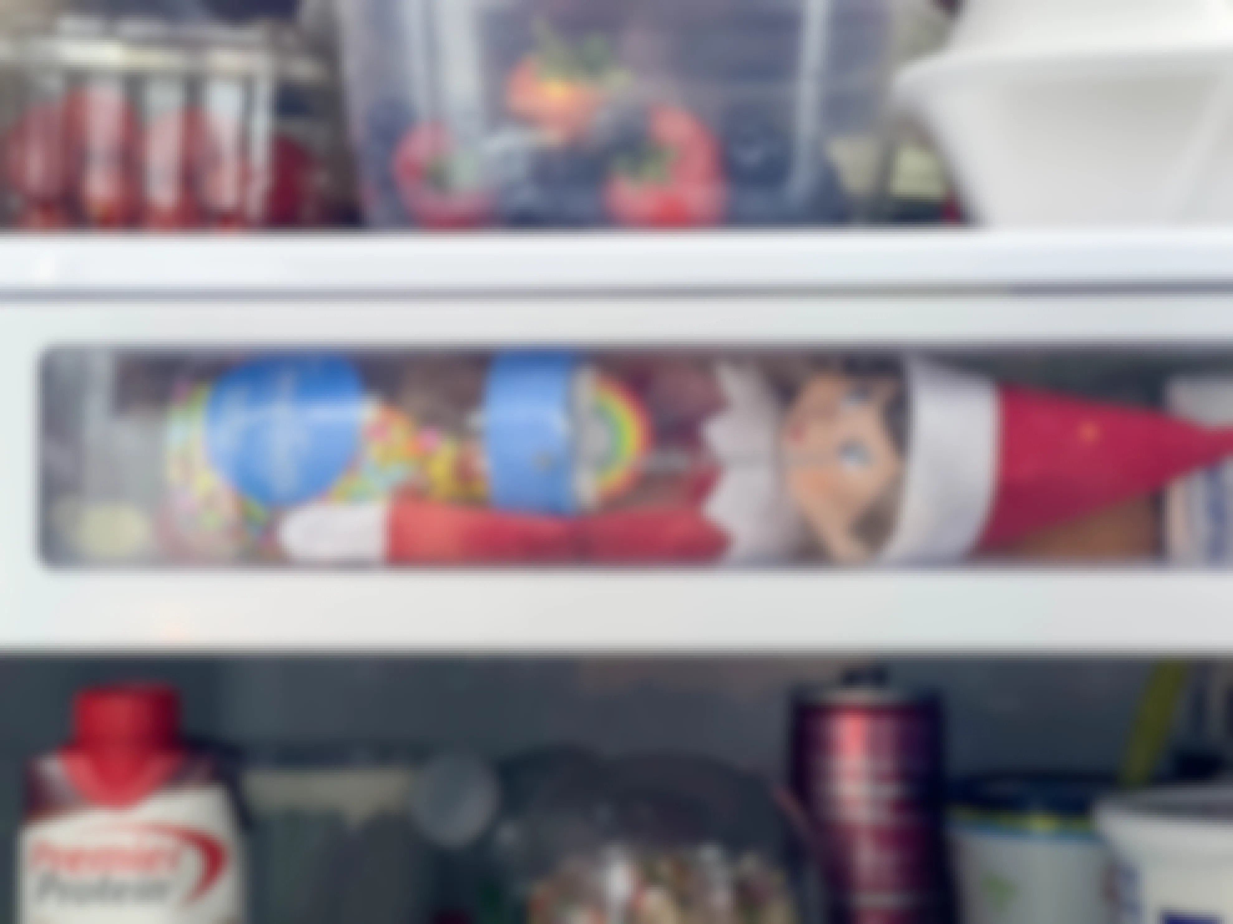 an elf on the shelf doll inside a fridge drawer holding sprinkles