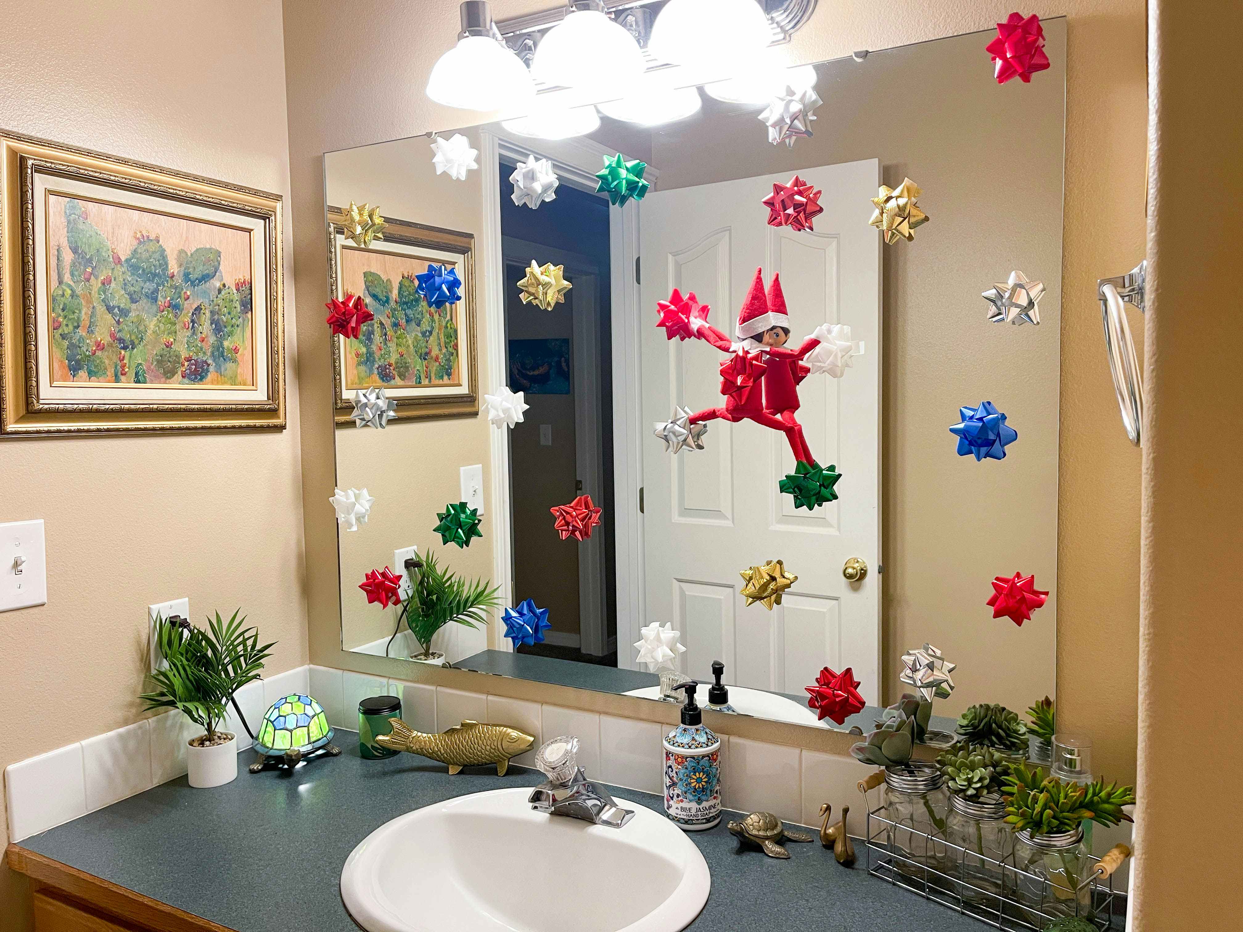 elf on the shelf doll climbing bathroom mirror with Christmas bows on mirror 