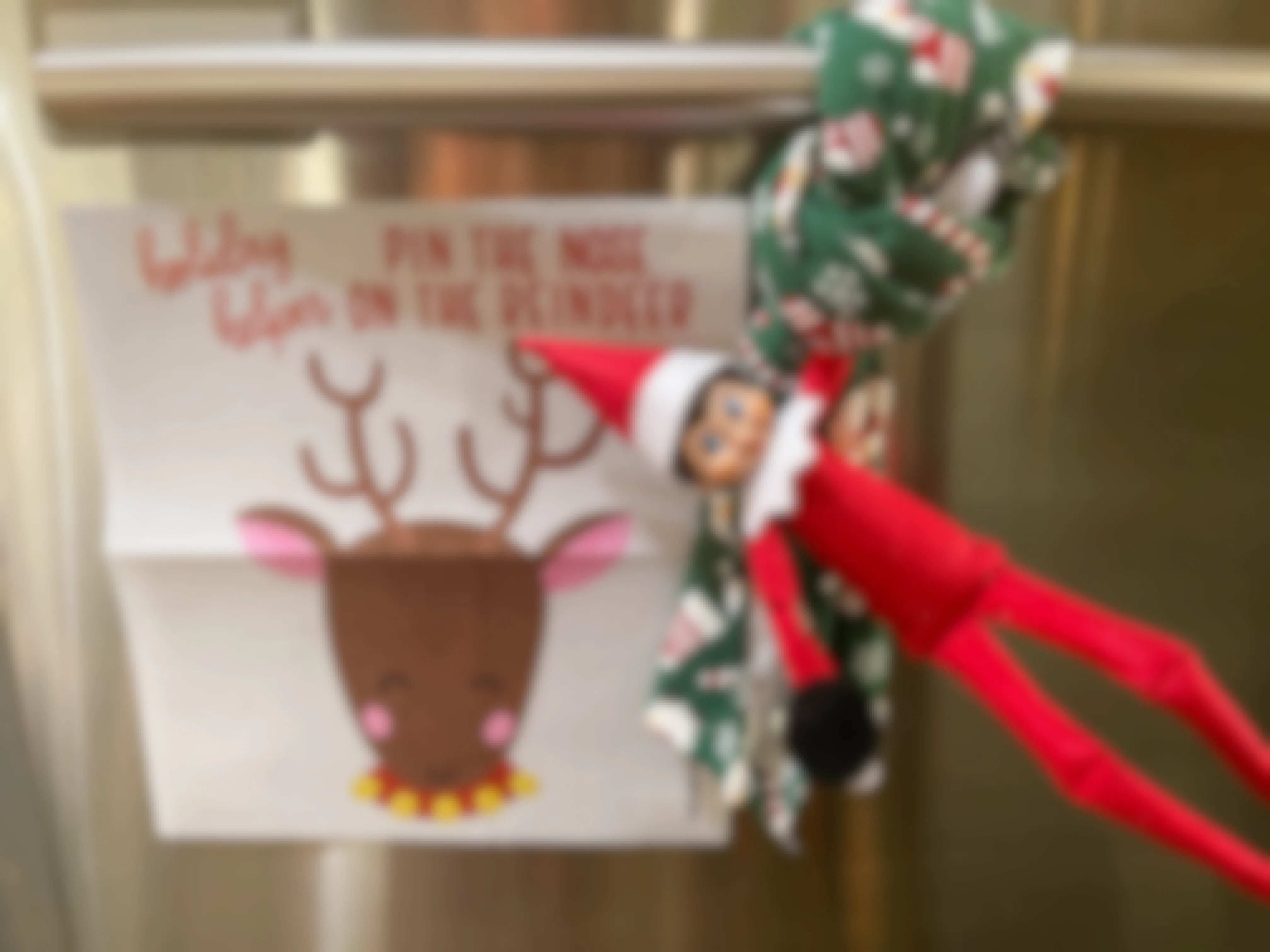an elf on the shelf doll playing pin the nose on the reindeer holding on a kitchen towel