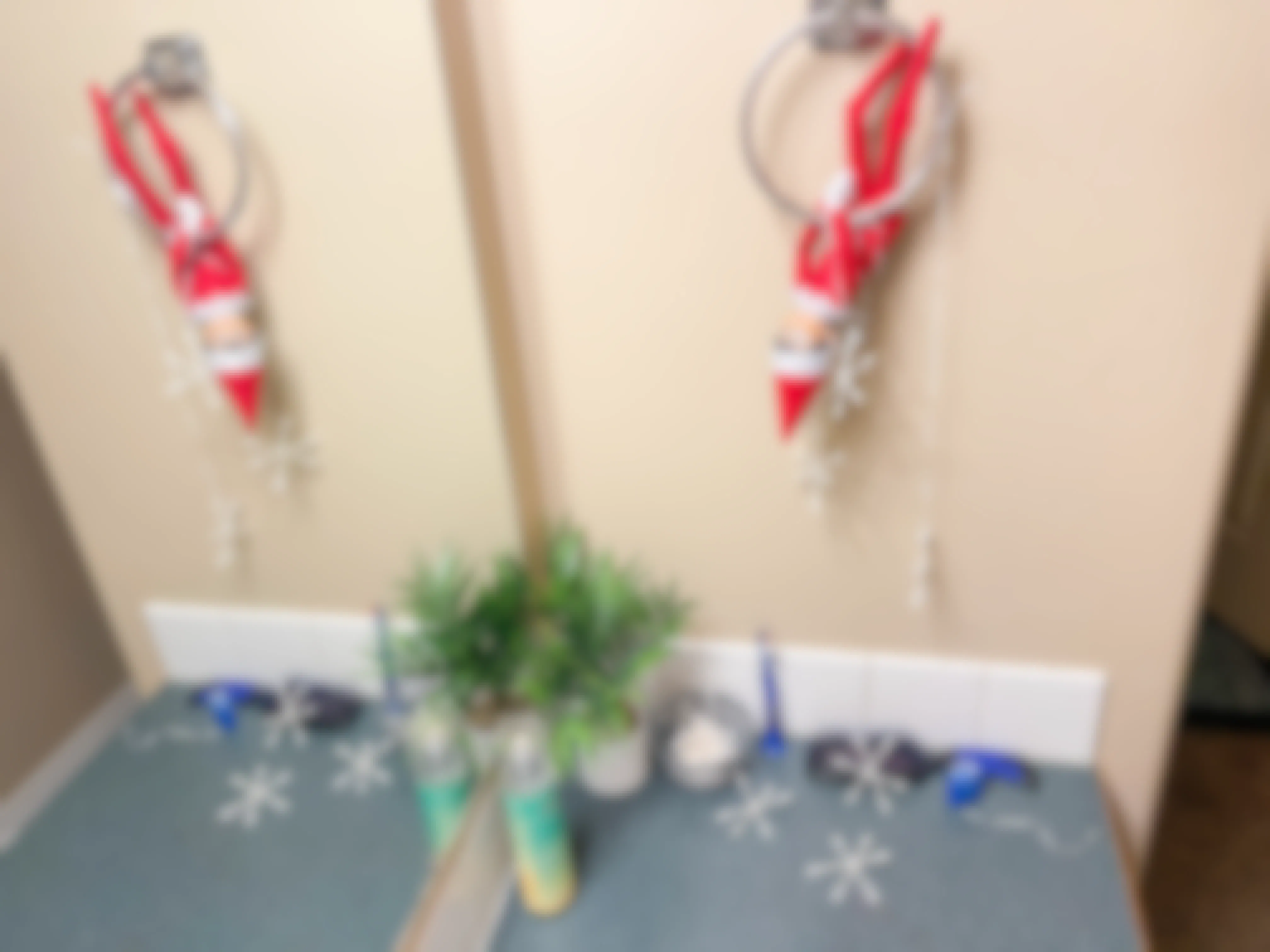an elf on the shelf doll hanging upside down on towel ring in bathroom with qtip snowflakes around counter