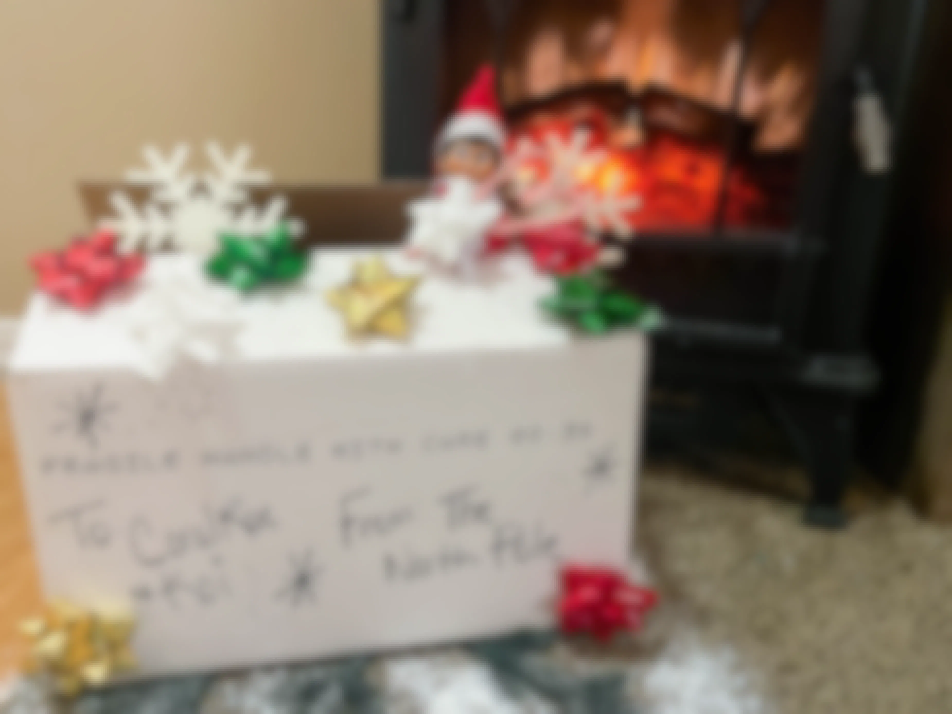 elf on the shelf doll peaking out of a box from the north pole in front of a fake fireplace 