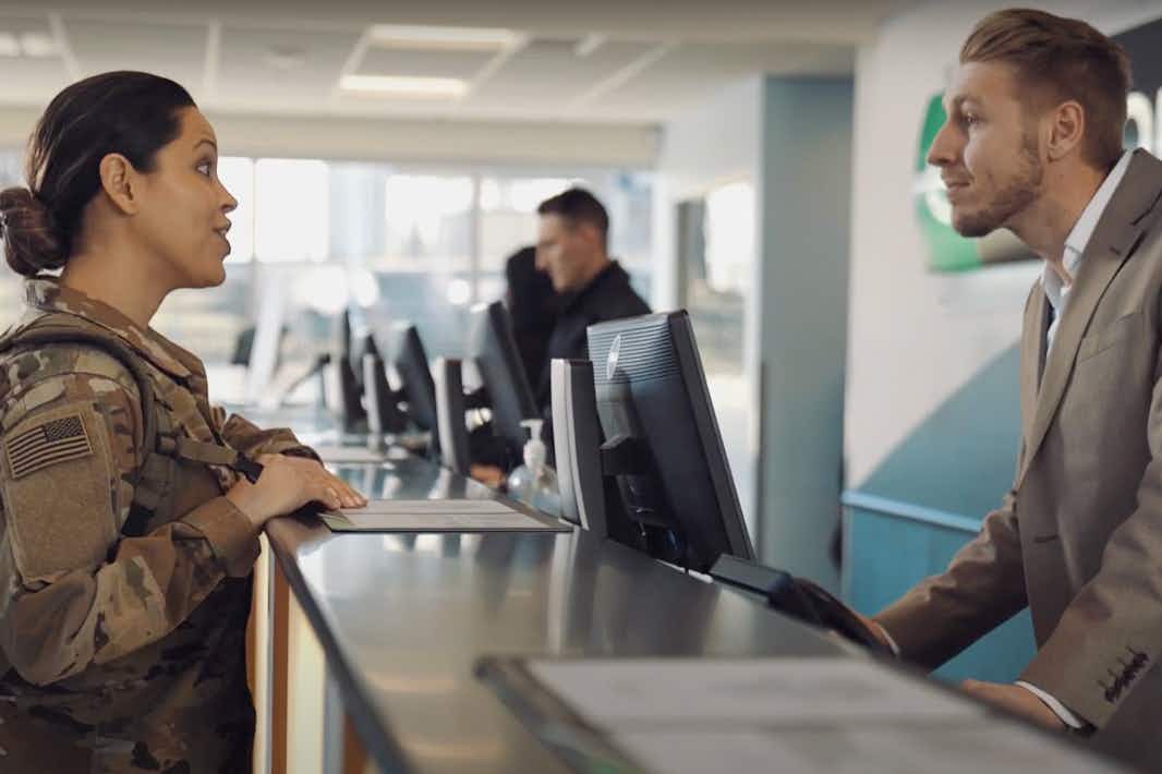 A person in military uniform talking to an Enterprise employee at the front desk