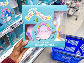 Someone holding a pair of Squishmallow plush headphones in front of a Five Below basket and shelf