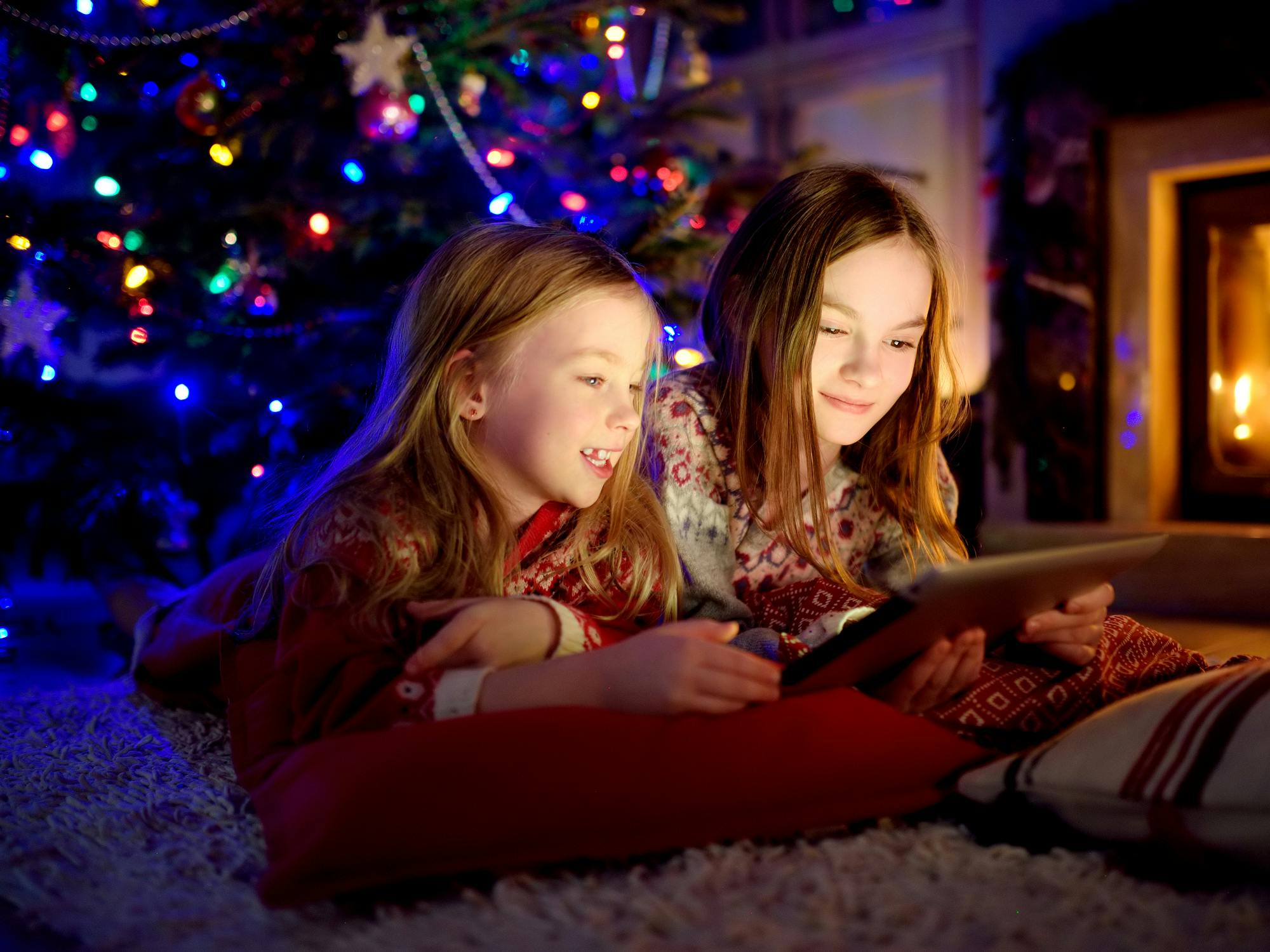 girls lying on living room floor watching christmas movie on tablet