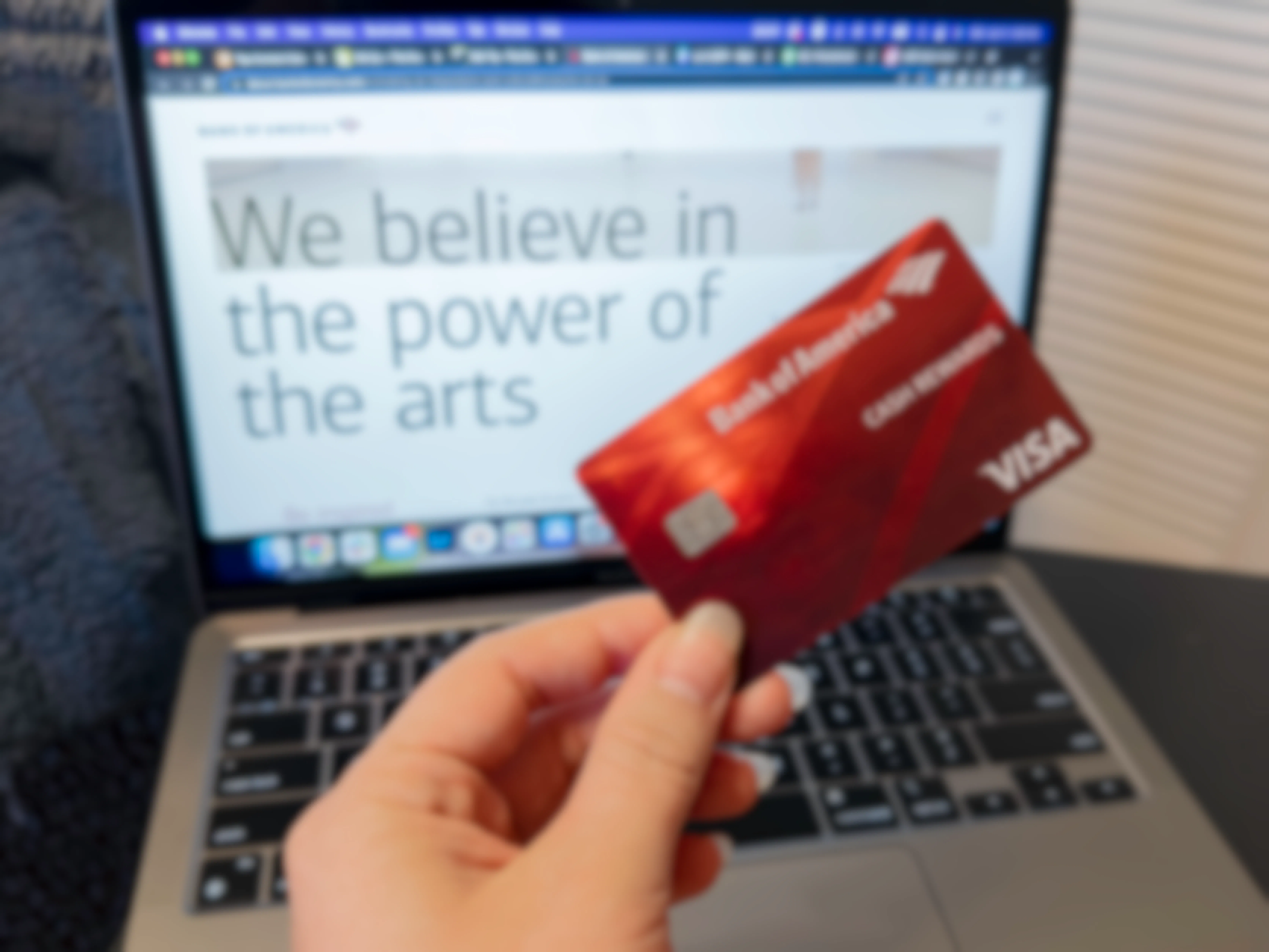 Someone holding their Bank of America card in front of a laptop displaying the information page about their Museums on Us program