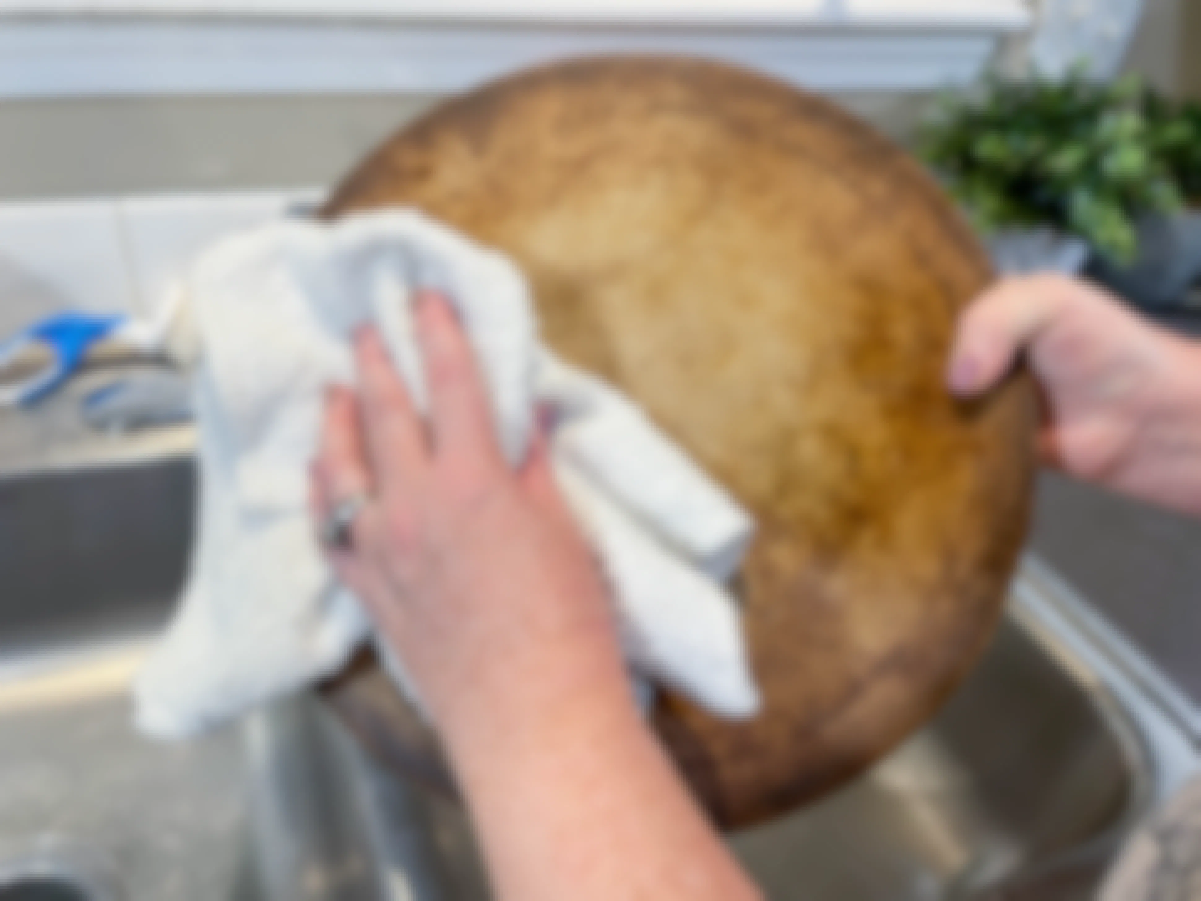 a person drying a pizza stone with a soft cloth over a sink