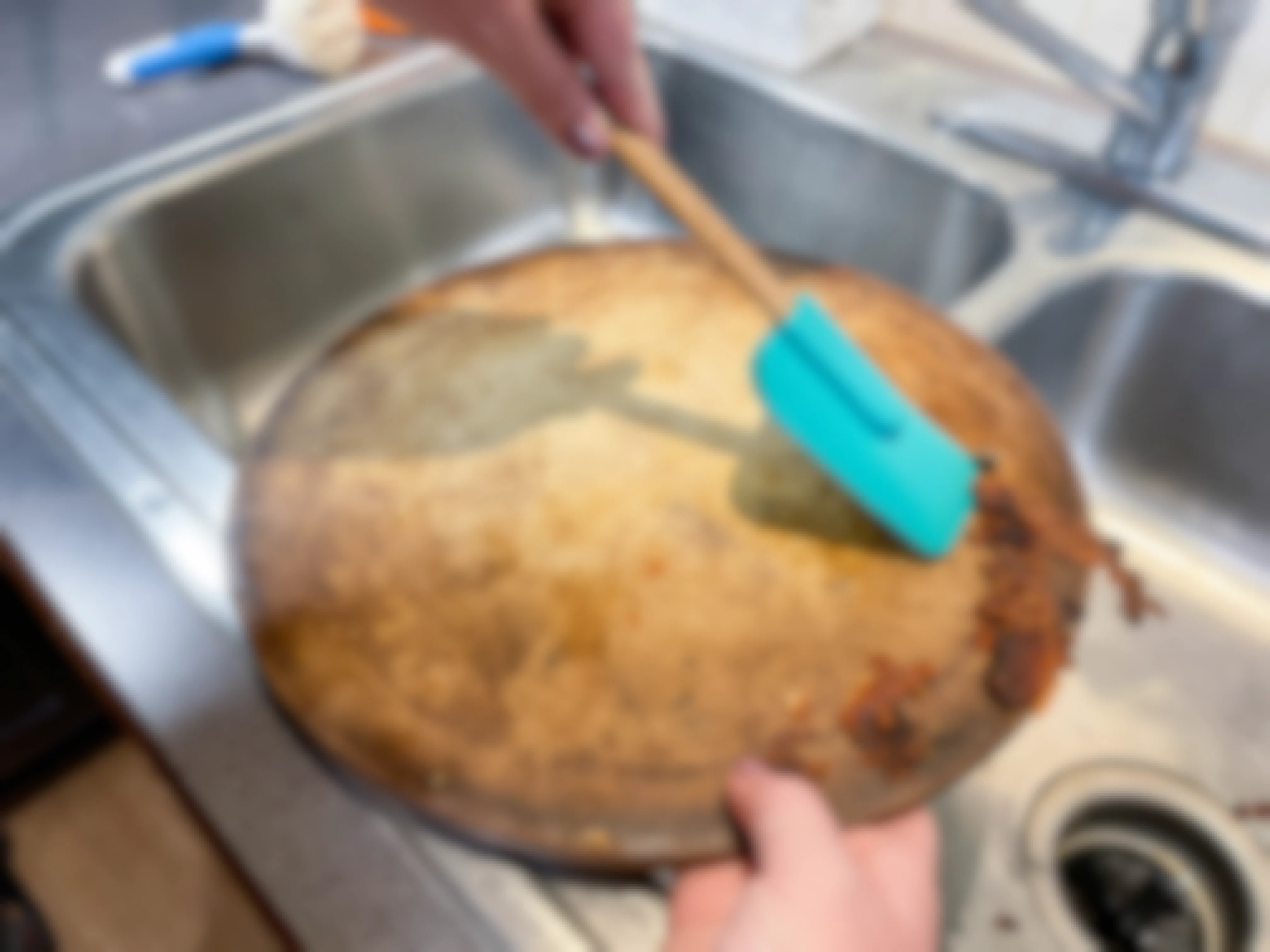 a person using a plastic spatula to scrap off baked cheese into the sink 