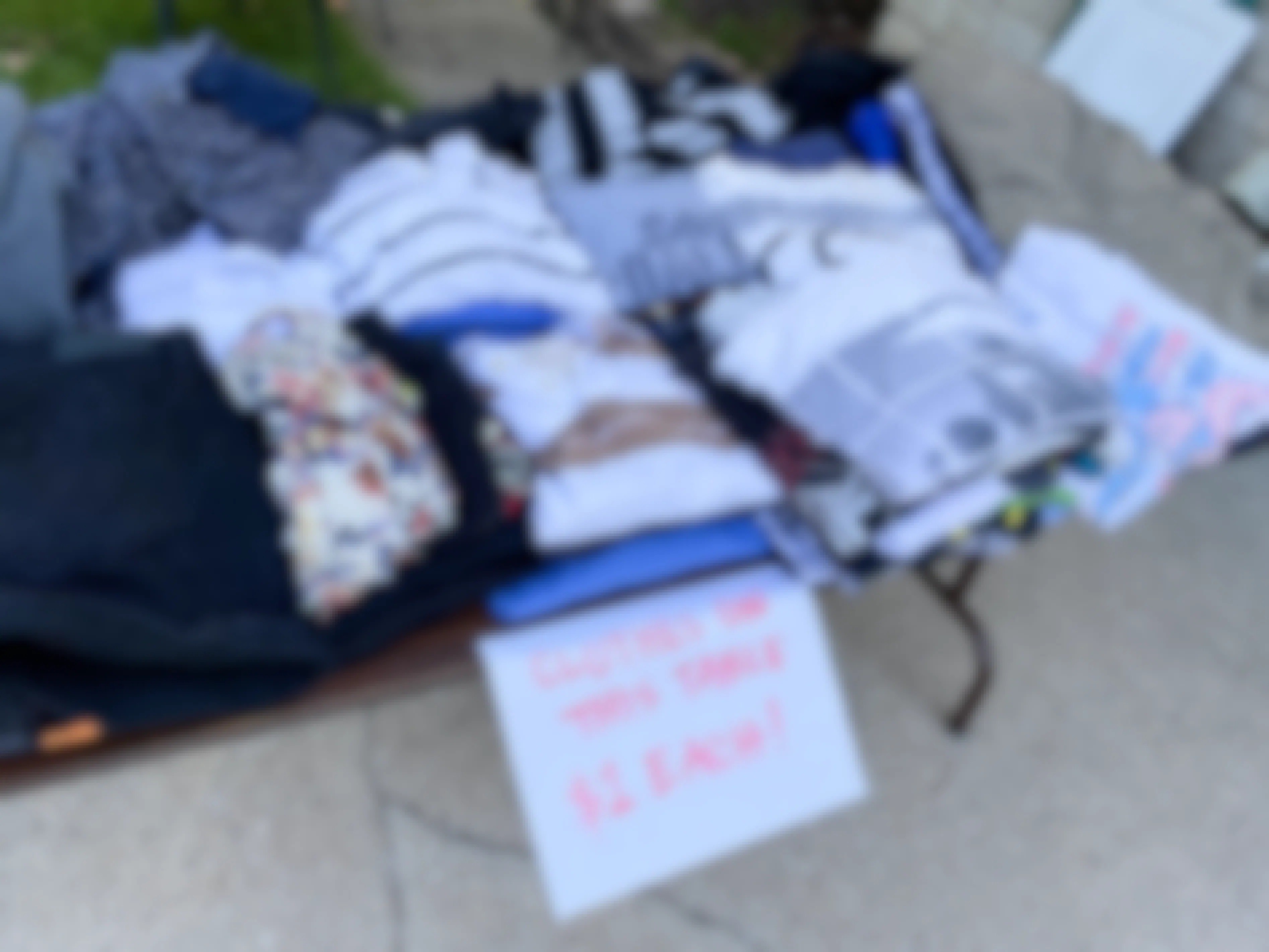 A table of clothing at a garage sale with a sign marking them as $1 each