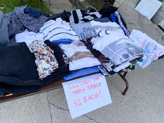 A table of clothing at a garage sale with a sign marking them as $1 each