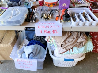 Tables of items for sale at a garage sale and signs advertising their prices