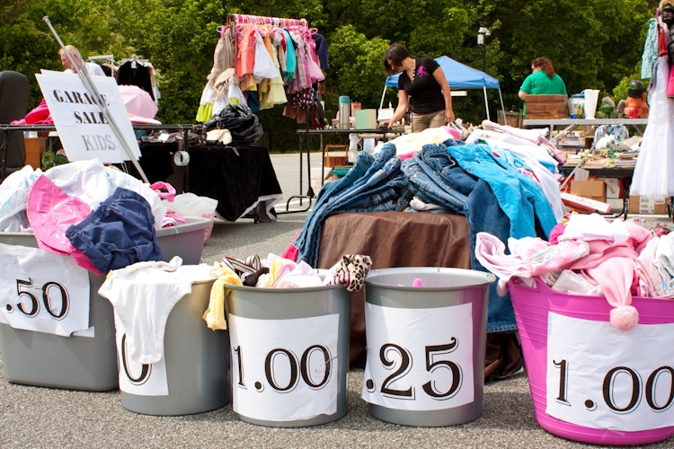 Bins at a garage sale with price signs on the going up in 25 cent increments 