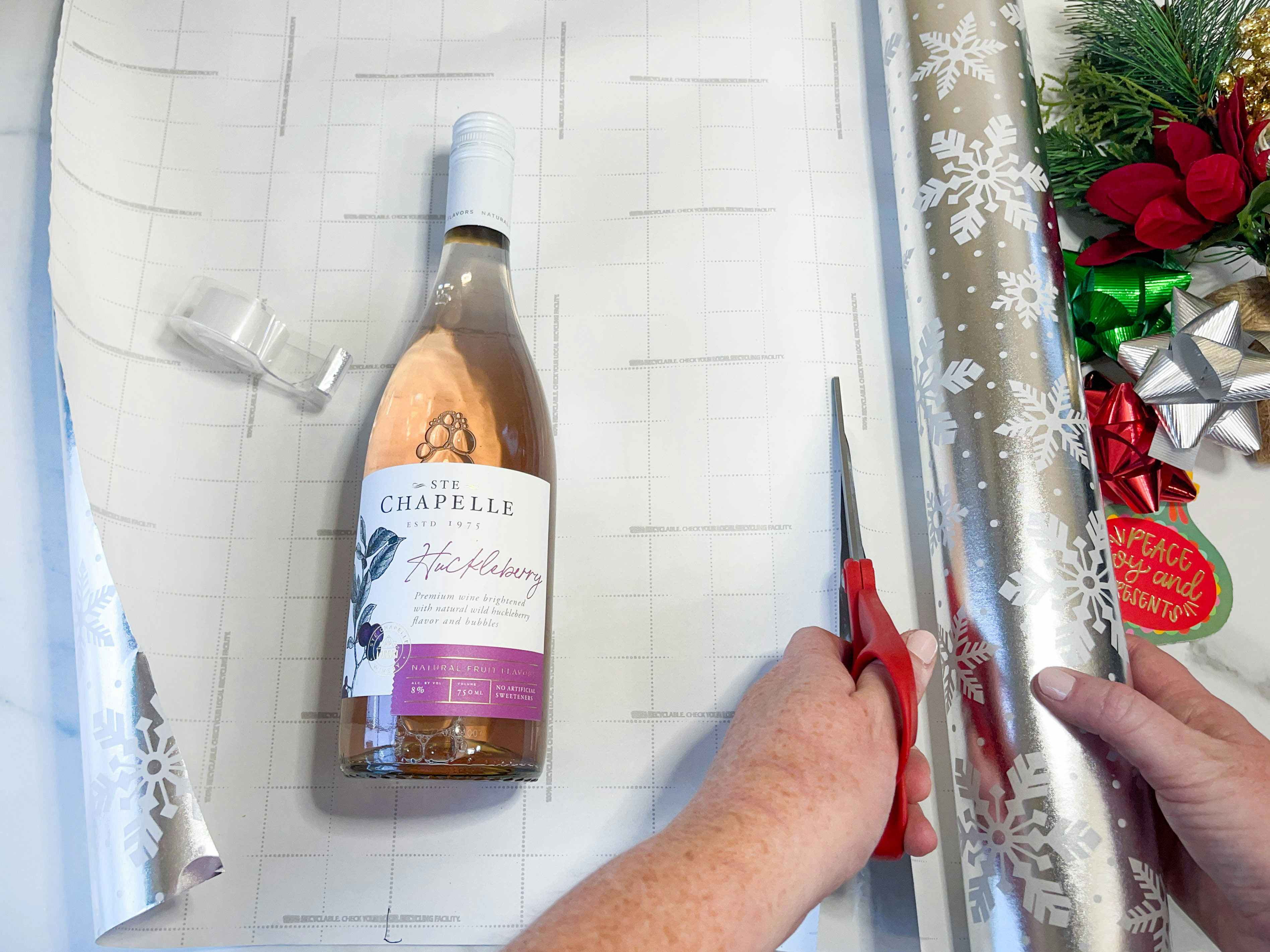 a person cutting wrapping paper about to wrap a bottle of wine 