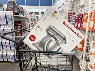A Kitchenaid Artisan mixer sitting in a shopping cart with other kitchen products in the background