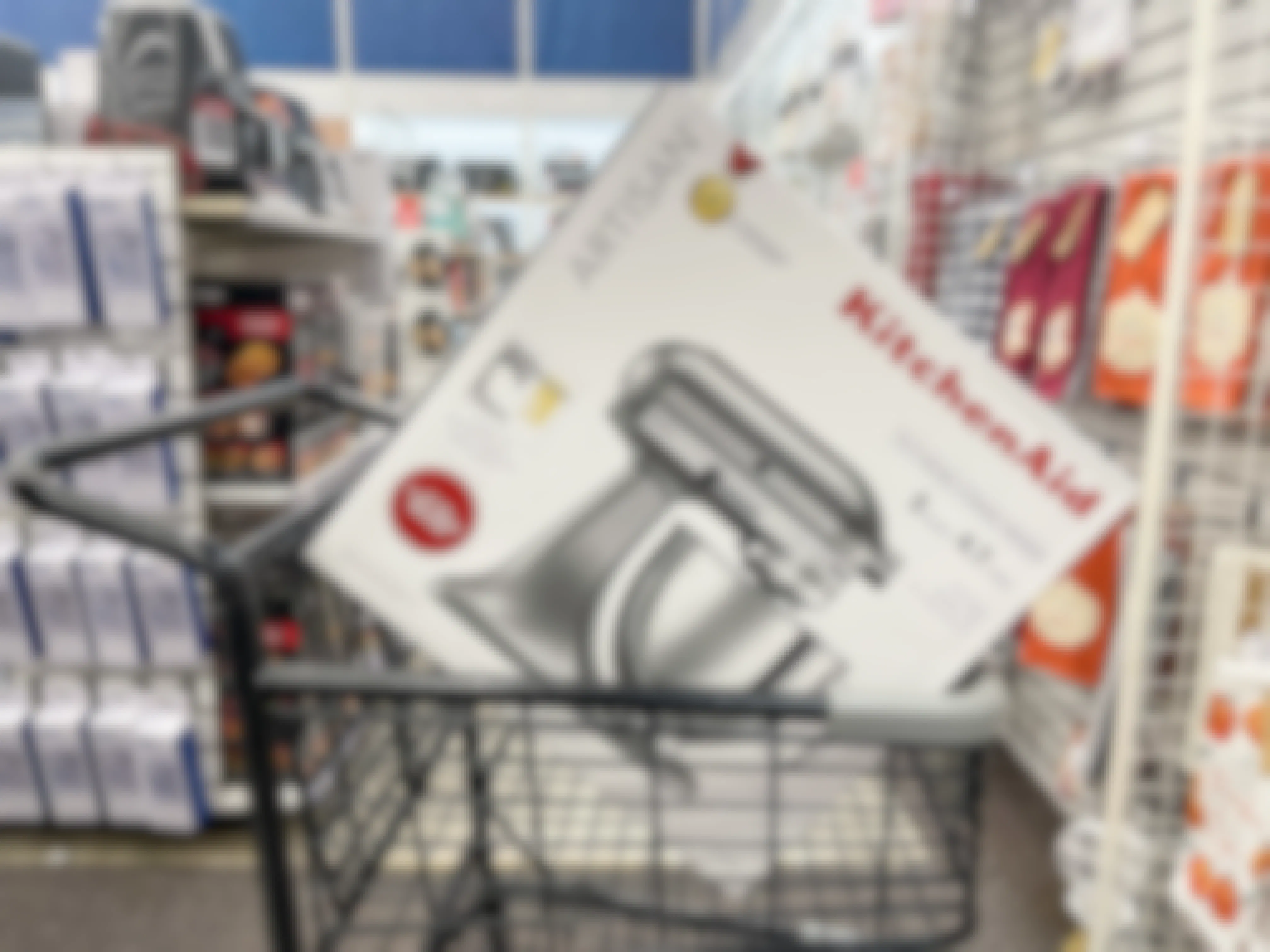 A Kitchenaid Artisan mixer sitting in a shopping cart with other kitchen products in the background