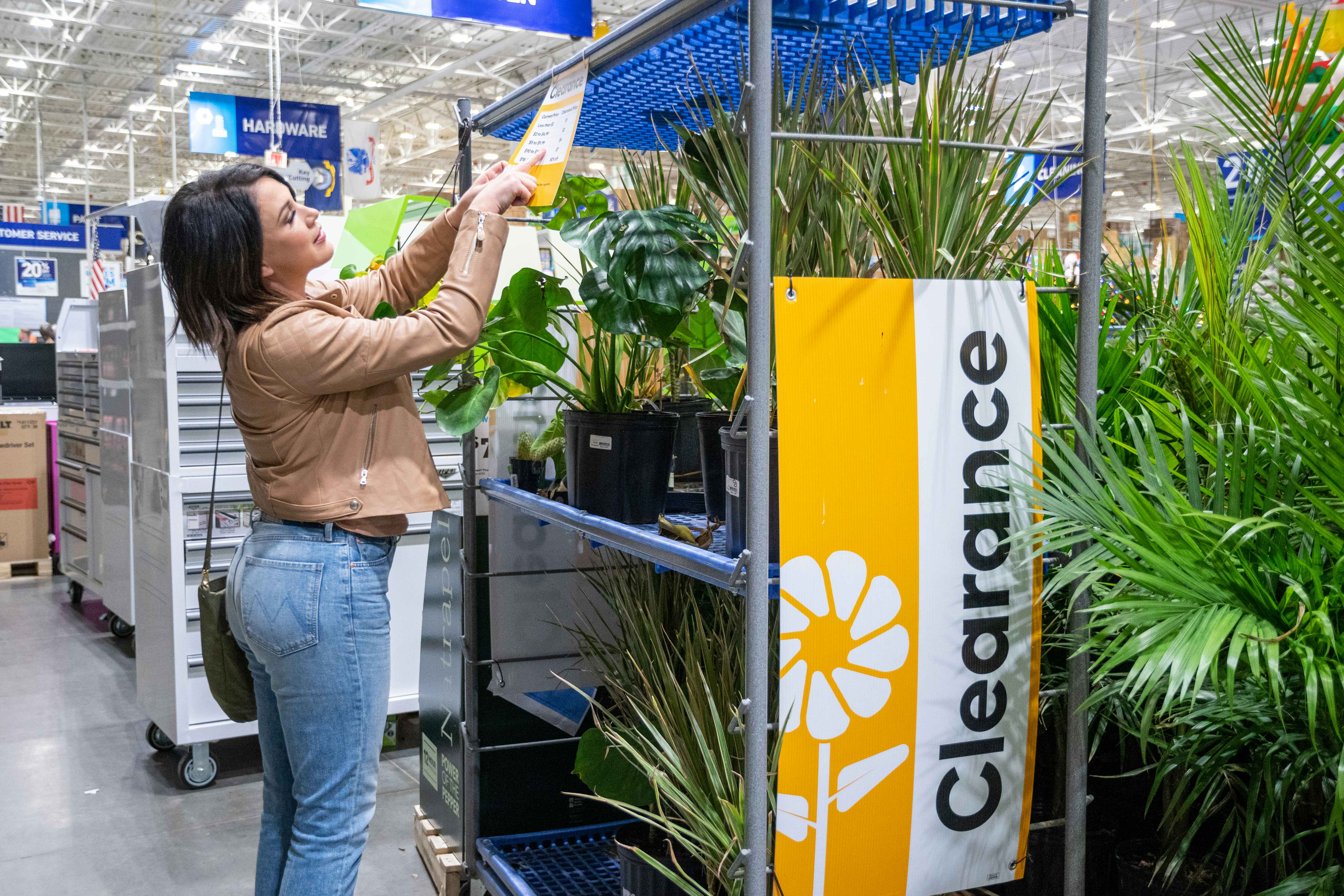 A person looking at the prices listed on a Clearance shelf of plants at Lowe's