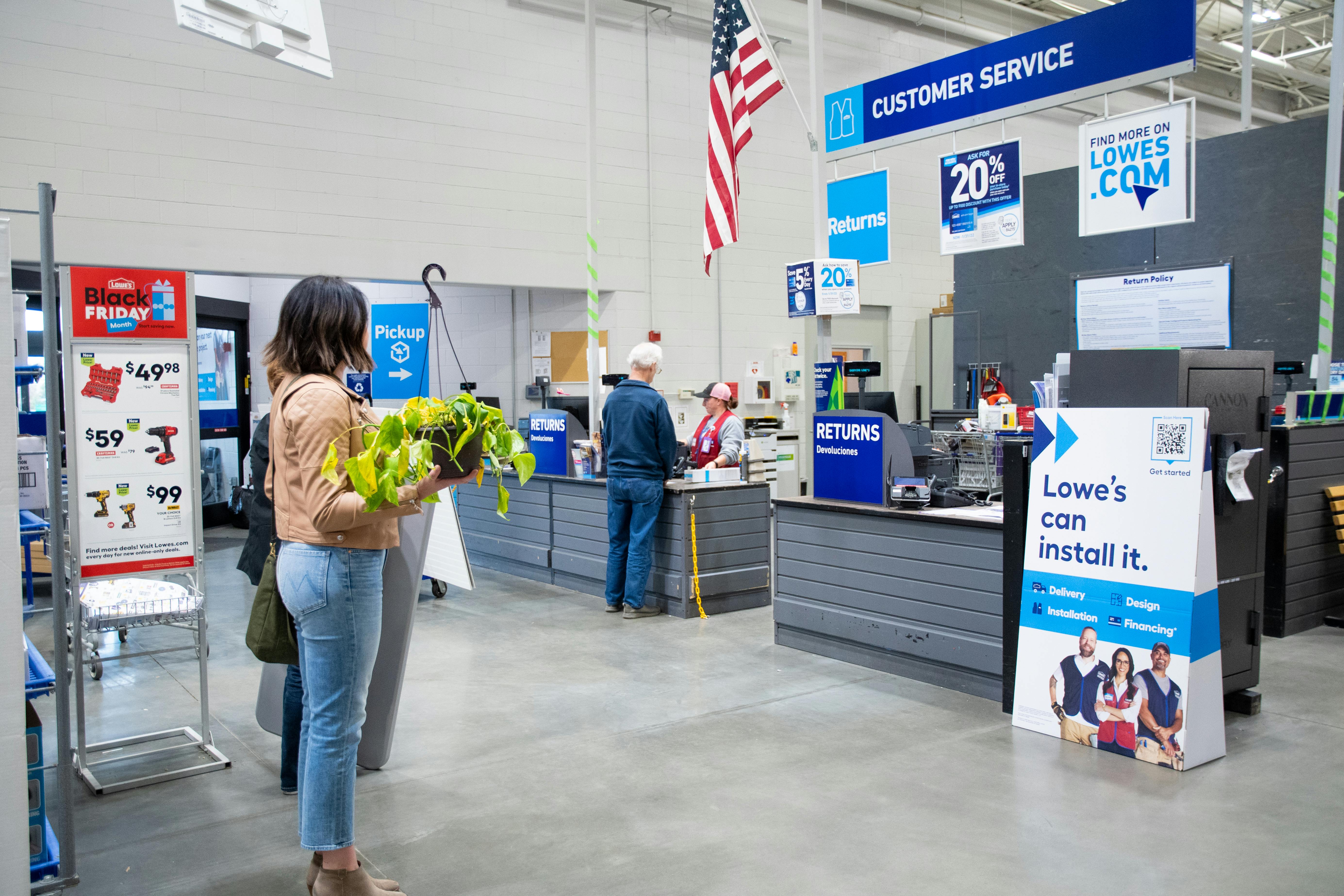 a woman standing in line holding a plant waiting to return it at Lowe's