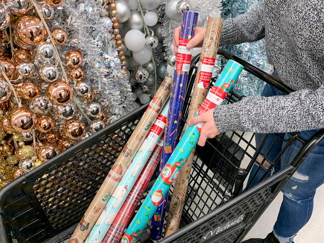 A person putting Christmas wrapping paper in a shopping cart