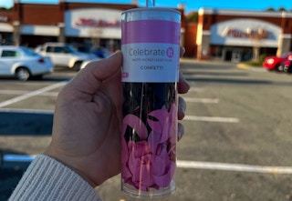 someone holding a container of pink confetti