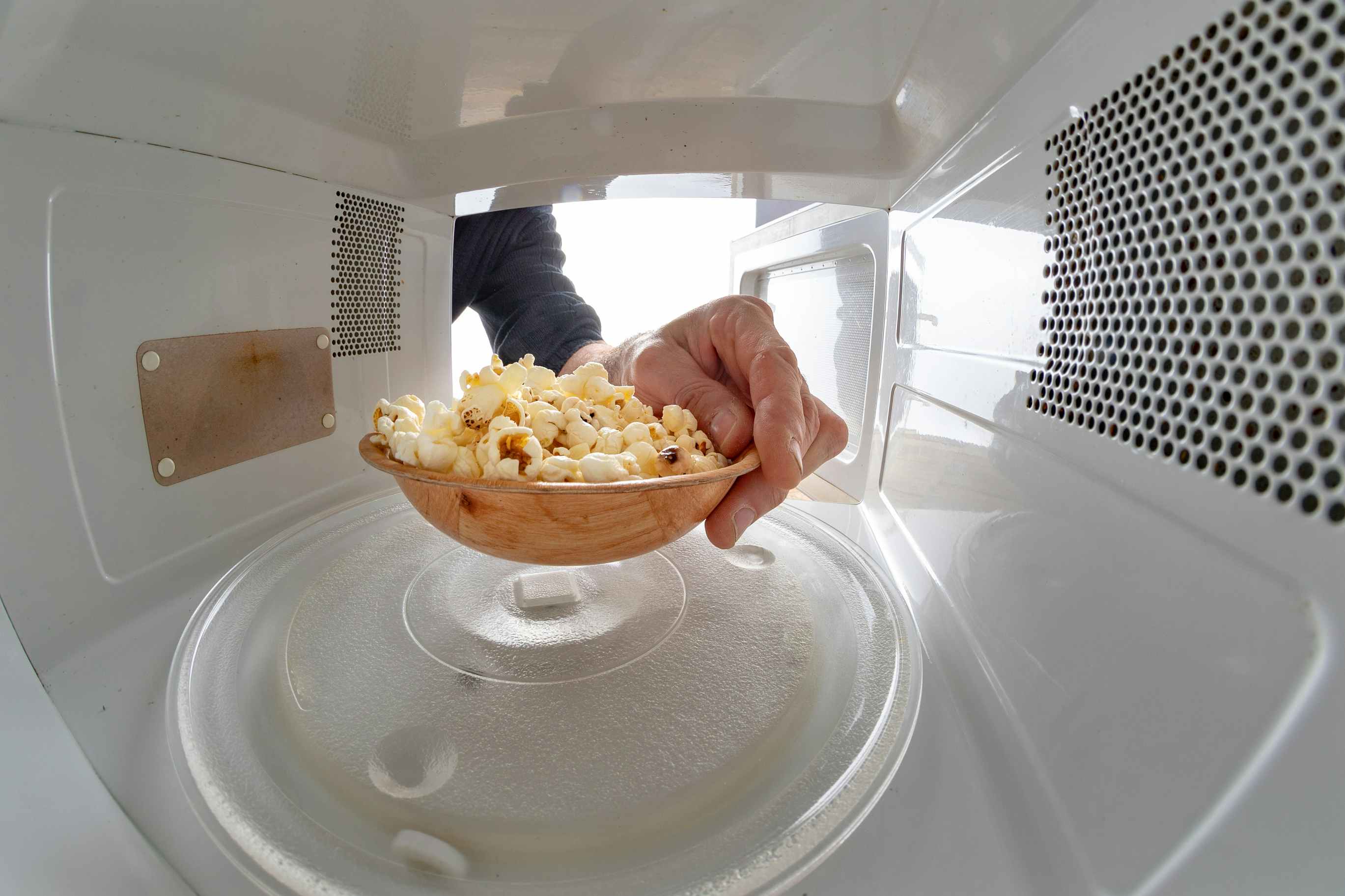 A person placing a bowl of already-popped popcorn into a microwave