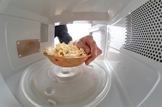 A person placing a bowl of already-popped popcorn into a microwave