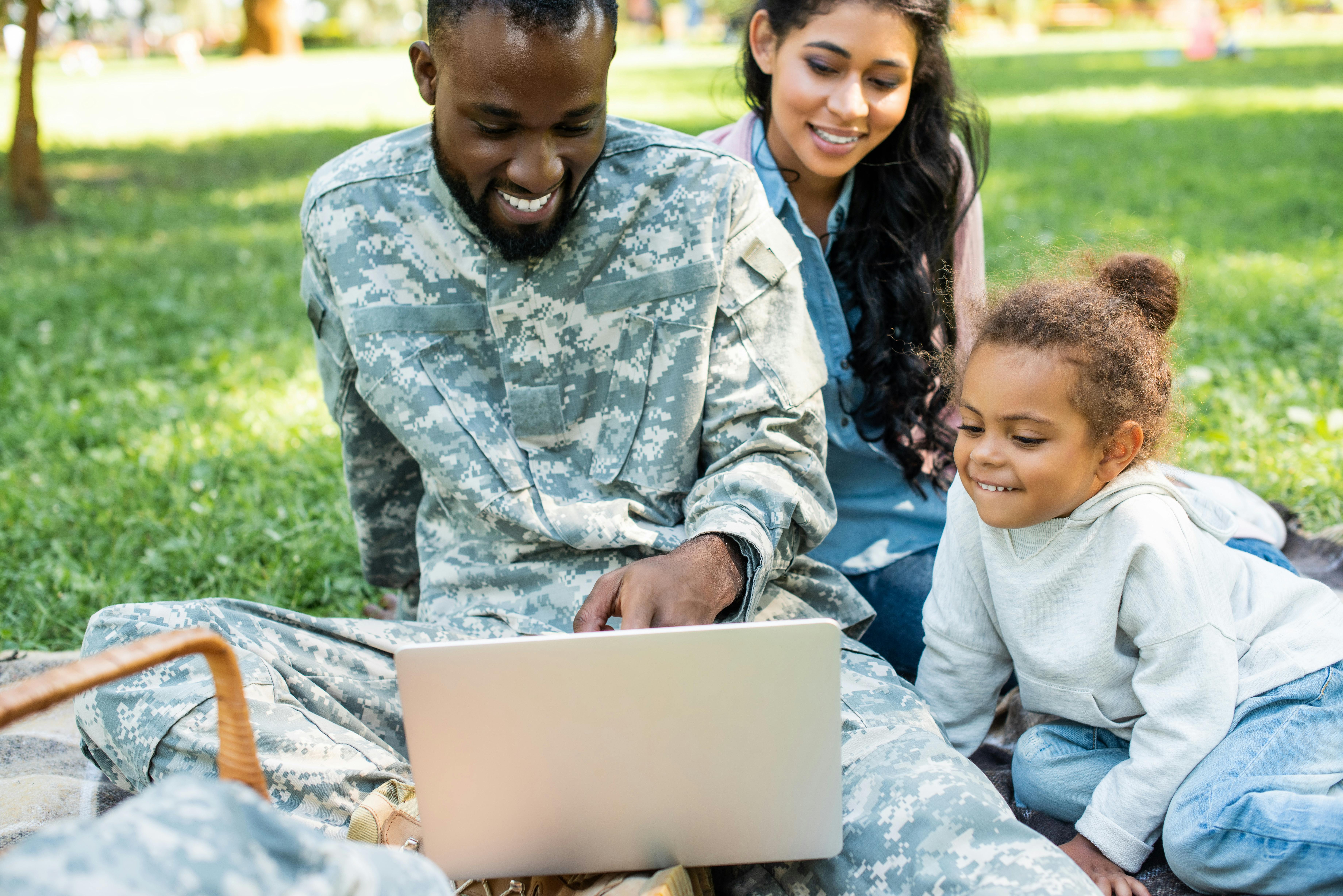 A family sitting on a lawn looking at a laptop computer