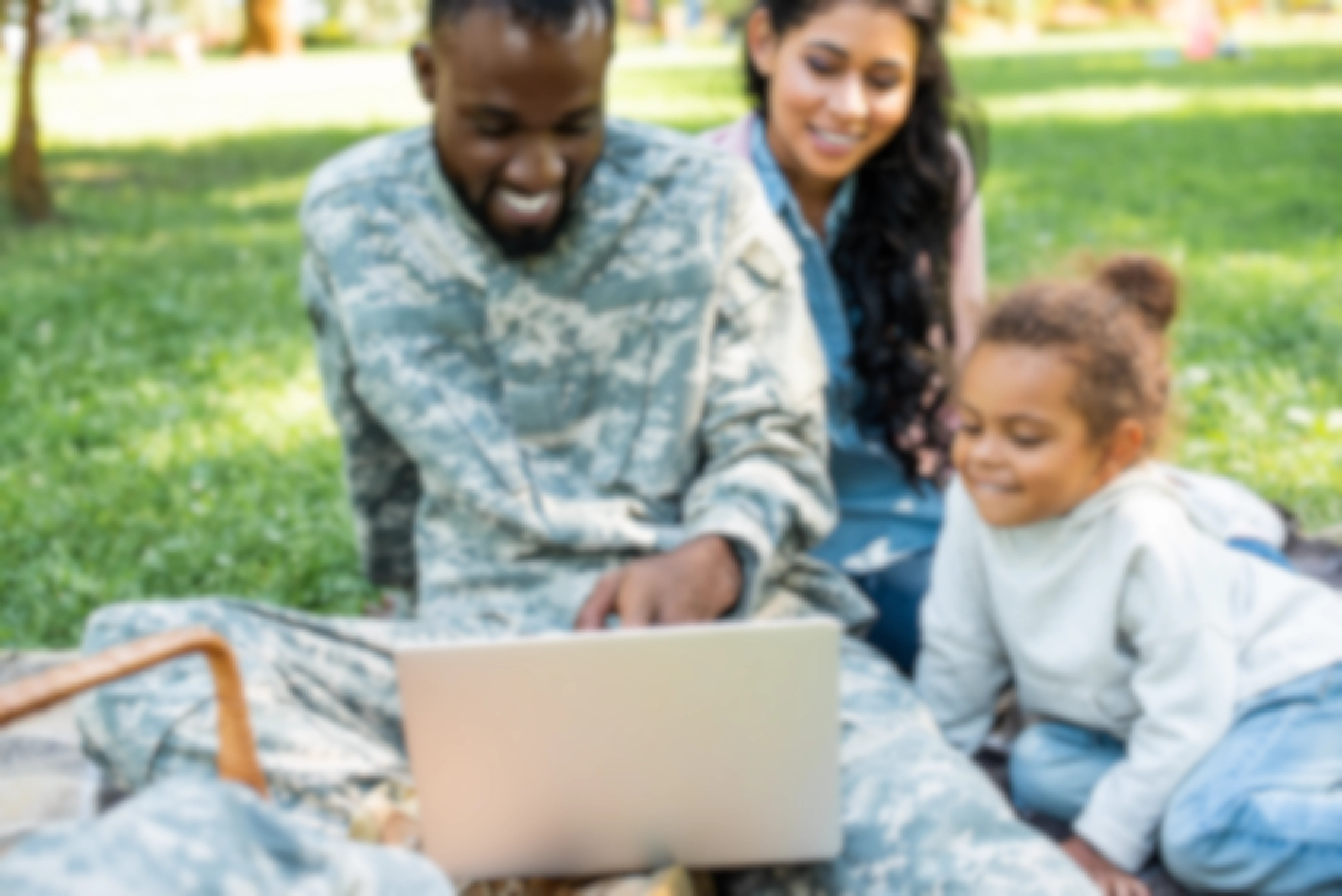 A family sitting on a lawn looking at a laptop computer