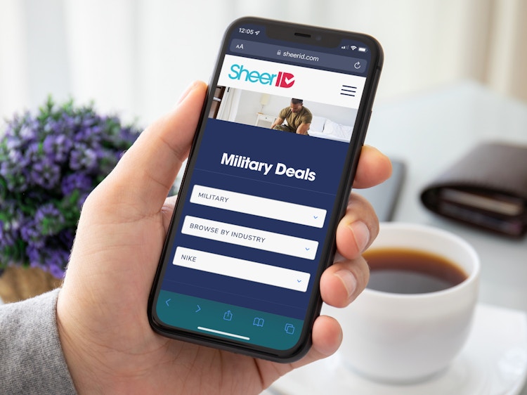 A person holding a cell phone displaying the SheerID Military discount offer search page