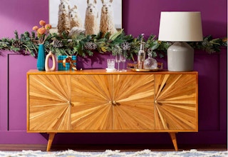 Brown wooden console table with christmas decorations against a purple wall.