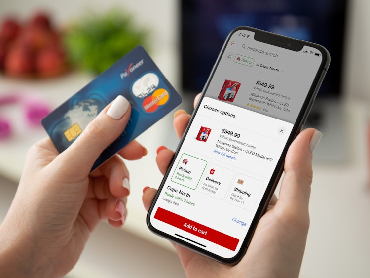 A person holding a credit card and looking at the OLED Nintendo Switch product page on the Target mobile app displayed on their phone