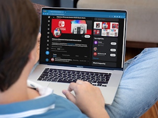 nintendo switch oled restock - A young person looking at the Twitter profile of SwitchStockNews on their laptop