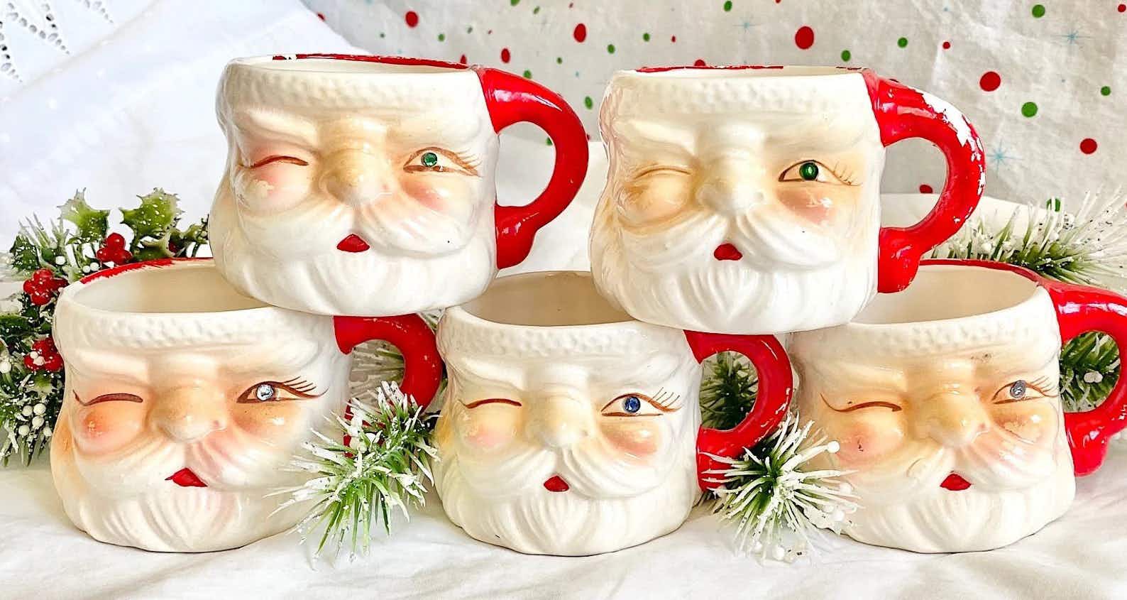 vintage santa mugs - A collection of Hand-Painted Winking Santa Face Mugs on a table decorated with holiday decorations