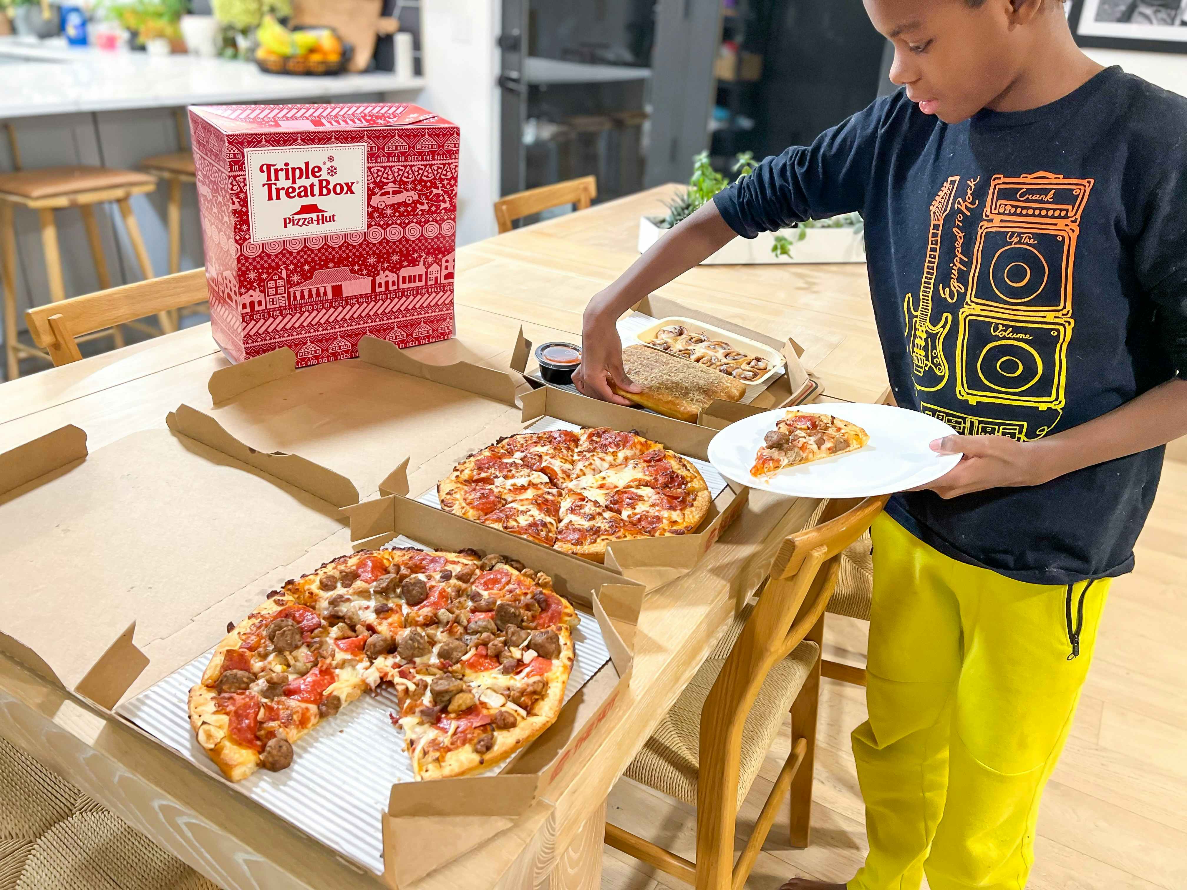 A young boy taking a slice of pizza from a box on a table