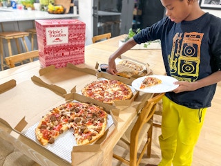A young boy taking a slice of pizza from a box on a table