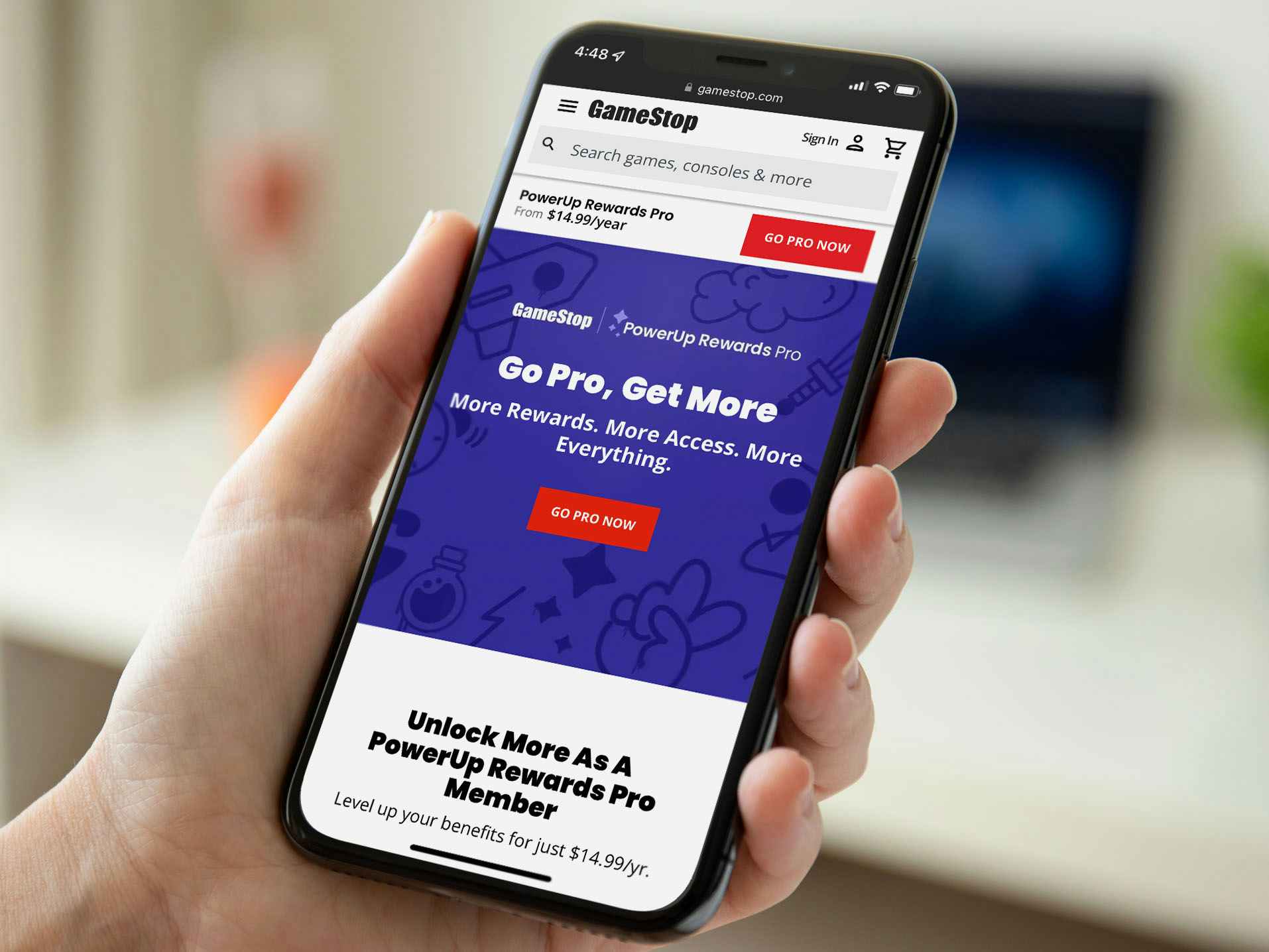 A person holding a cell phone displaying the GameStop Pro Rewards webpage