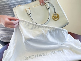 a person putting a michaels kors handbag in dust bag