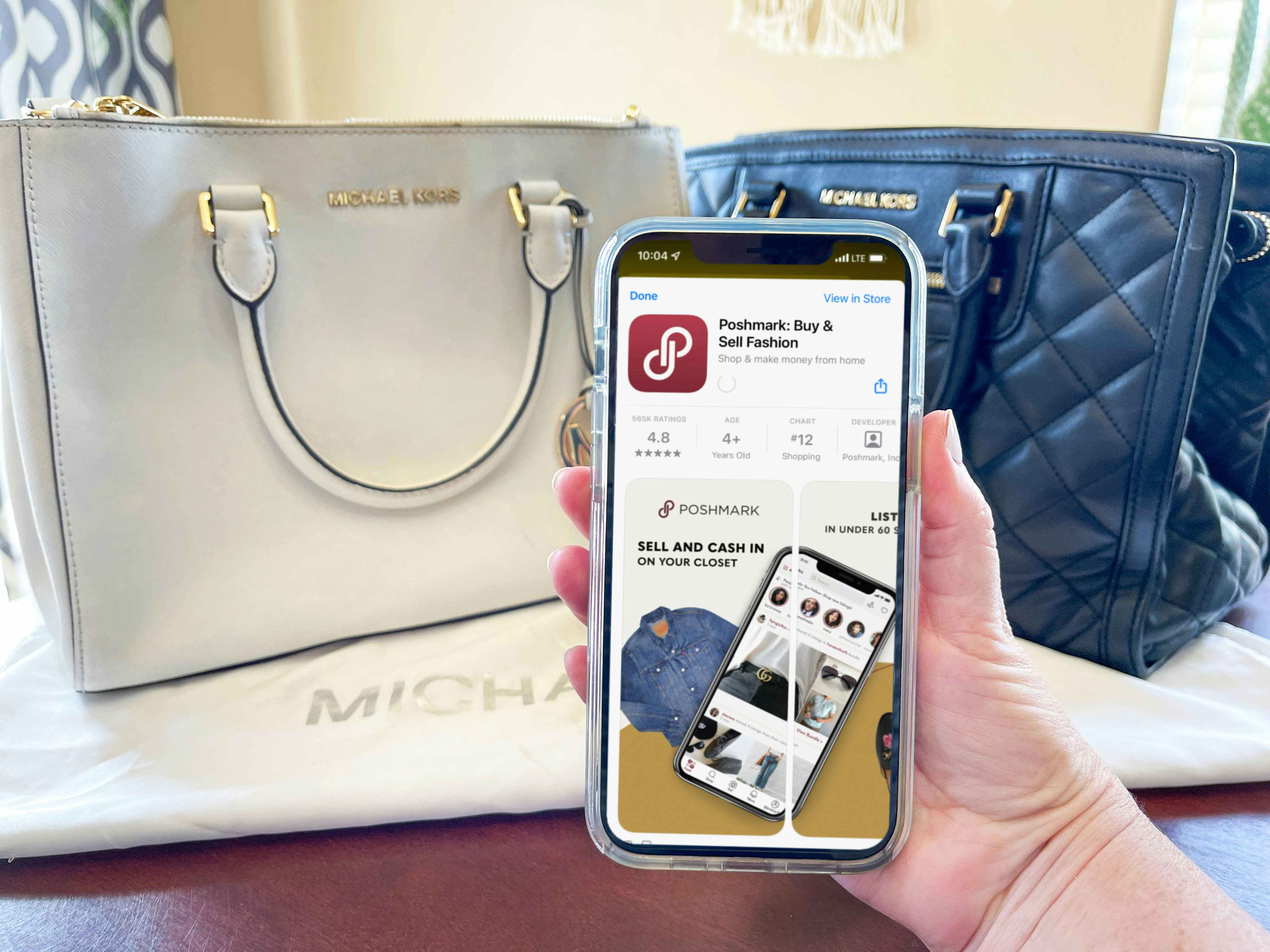 michael kors handbags on table with a person holding a sell phone with poshmark on screen 