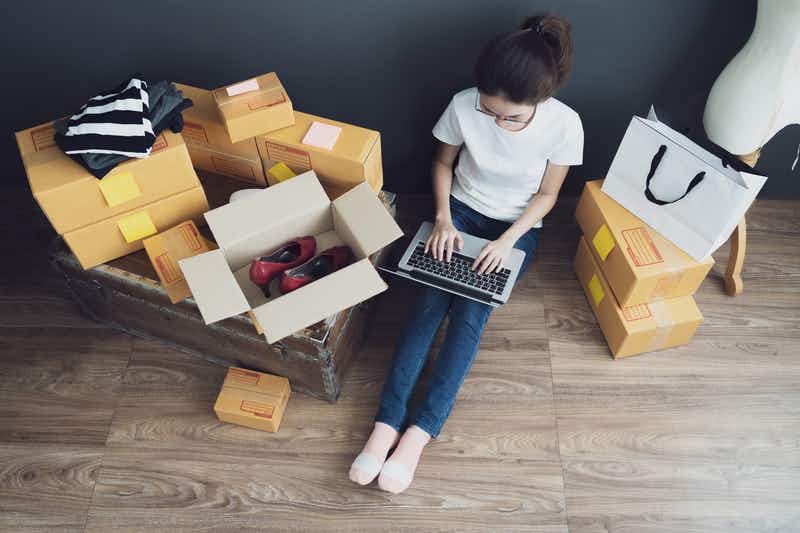 a woman sitting on the floor with a laptop near boxes with clothing 