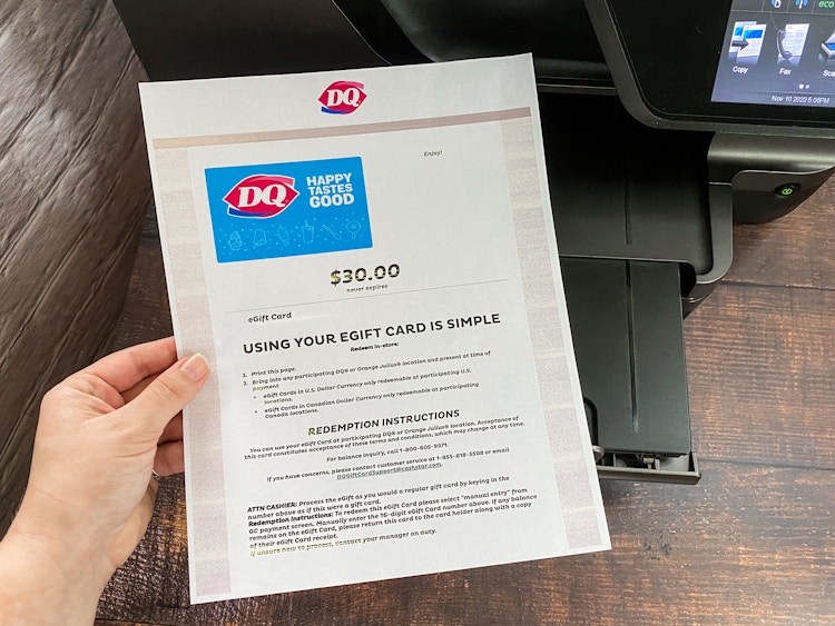 a person's hand holding a printed out egift card from dairy queen in front of a printer 