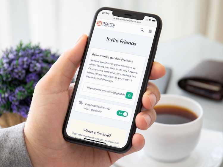 A person holding a cell phone displaying the Invite page on the Scott's Cheap Flights website